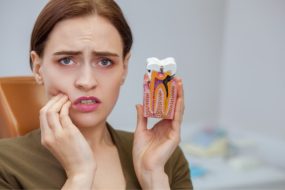 Frau mit Sekundärkaries halt das Modell eines kariösen Zahns
